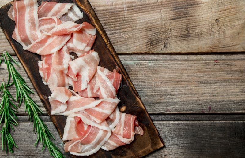 Raw bacon with fragrant rosemary. On a wooden background. Raw bacon with fragrant rosemary. On a wooden background